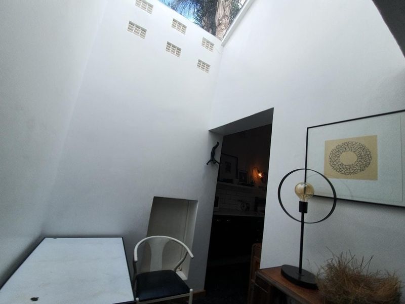 A small, open-air courtyard or light well featuring high white walls, ventilation blocks, and a skylight, providing natural light to the adjacent interior space.