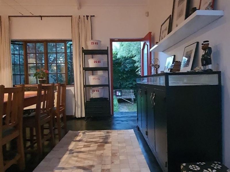 Dining area featuring painted concrete floors and timber-framed windows, with direct access to the rear garden through an open doorway.