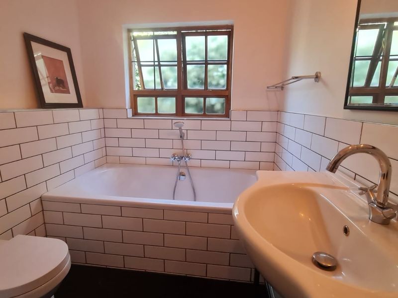 A well-maintained bathroom featuring subway tile wall cladding, a built-in bathtub with handheld shower, and a modern pedestal basin.