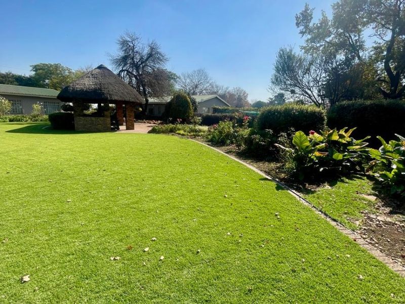 A well-maintained expansive garden featuring a traditional thatched gazebo, manicured lawn, and established garden beds.