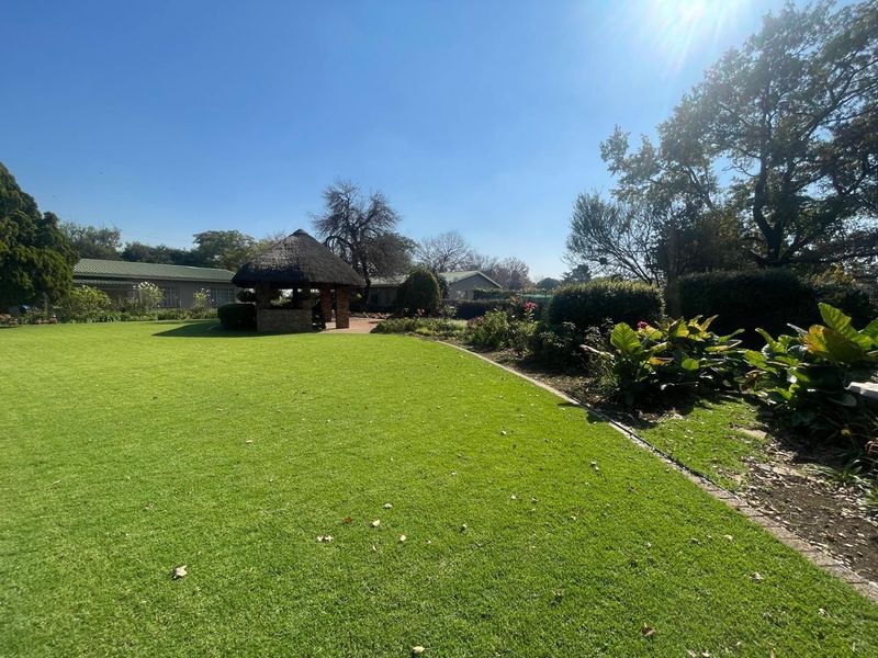 A well-maintained garden featuring a traditional thatched gazebo, expansive green lawn, and mature landscaping on a farm property.
