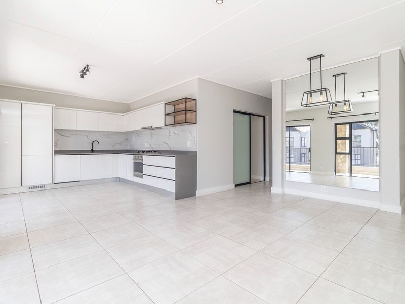 Modern open-plan kitchen and living area featuring sleek white cabinetry, stone countertops, integrated appliances, large format floor tiles, and a stylish mirrored feature wall.