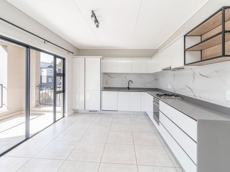 Modern kitchen featuring sleek white cabinetry, stone countertops, integrated appliances, and a marble-look splashback, with direct access to a private balcony.