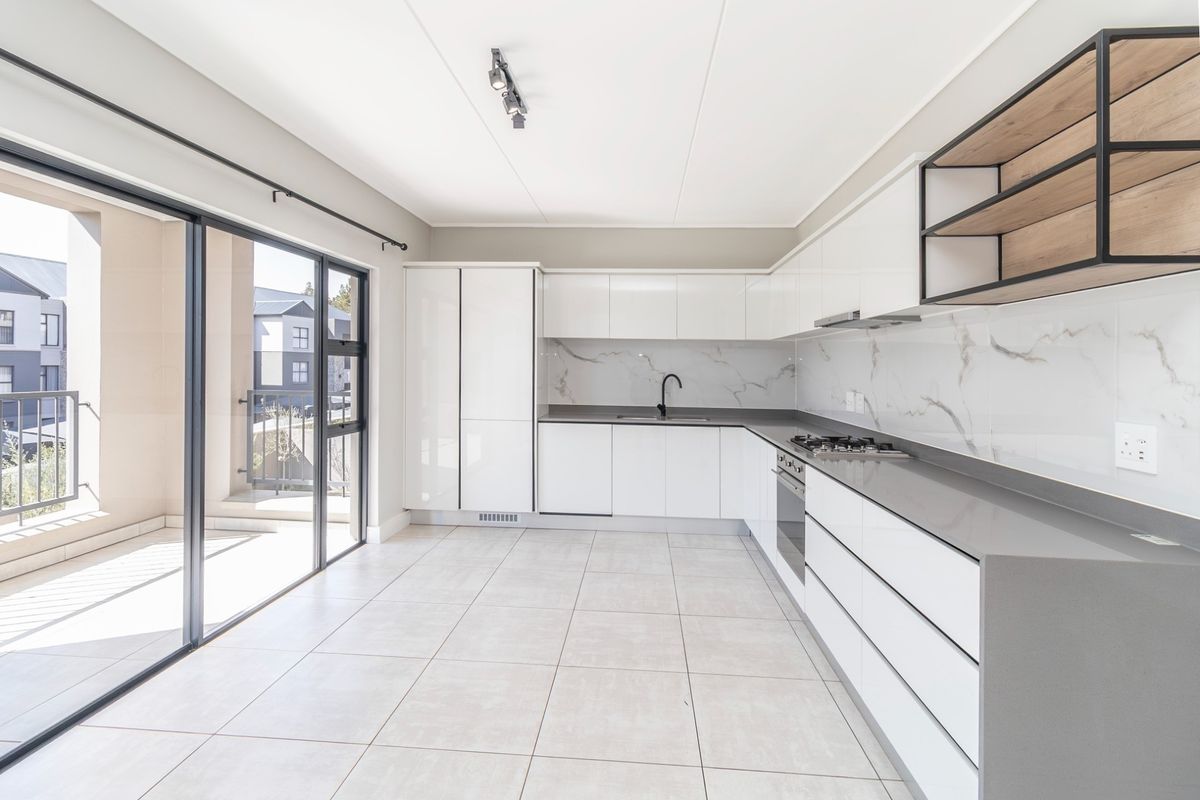 Modern kitchen featuring sleek white cabinetry, stone countertops, integrated appliances, and a marble-look splashback, with direct access to a private balcony.