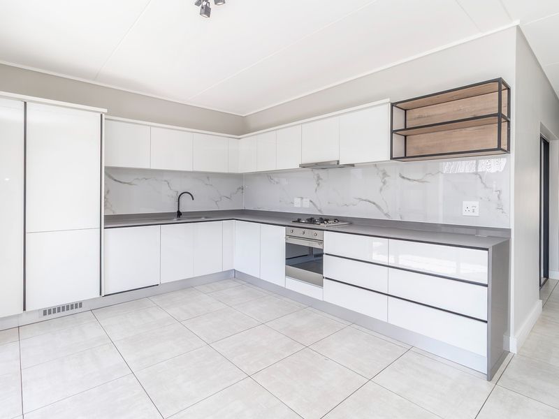 Modern kitchen featuring sleek white cabinetry, stone countertops, marble-look splashback, integrated oven, gas hob, and high-quality tiled flooring.
