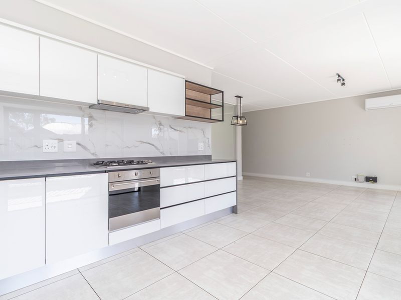 Modern open-plan kitchen and living area featuring sleek white cabinetry, stone countertops, gas hob, and tiled flooring in a bright, well-maintained space.