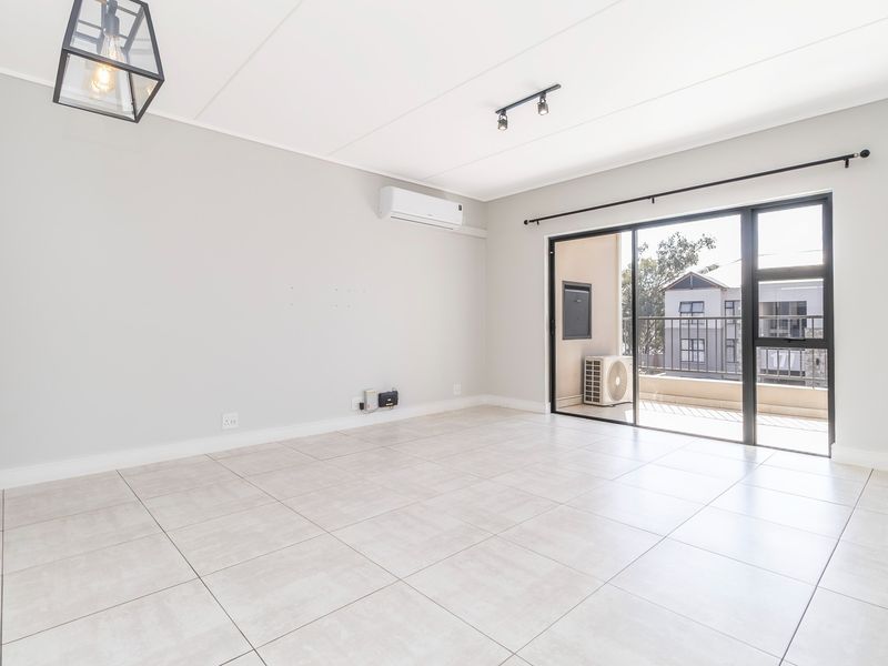 Bright and spacious open-plan living area featuring neutral tiled flooring, modern lighting, and direct access to a private balcony through sliding glass doors.