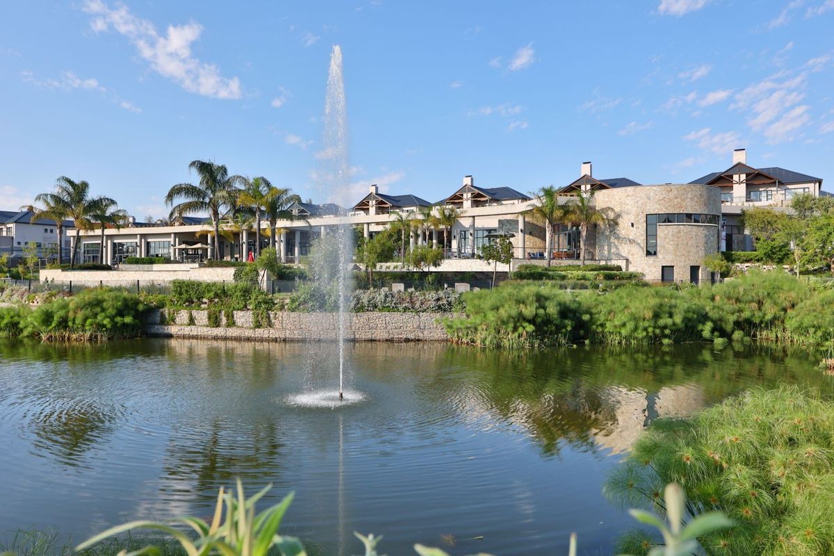 A scenic view of the apartment complex exterior featuring a landscaped garden, a central water fountain, and a tranquil pond.