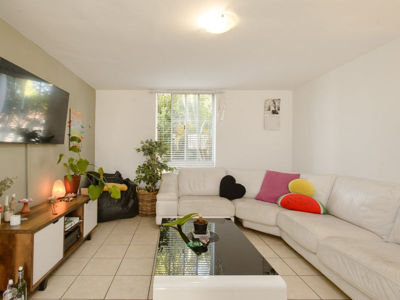 A functional living room featuring tiled flooring, a large window with venetian blinds, and a neutral wall finish.