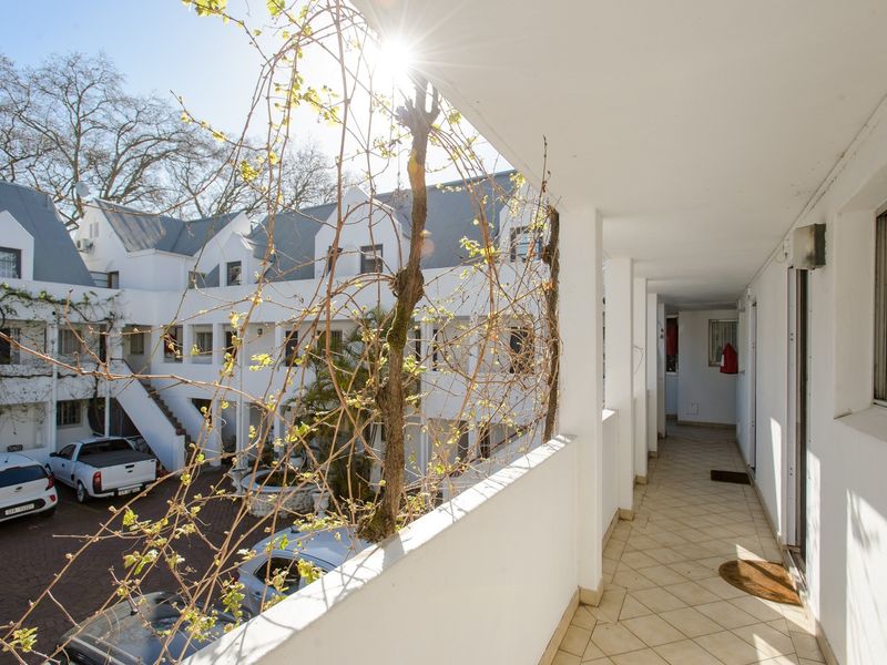 An open-air apartment balcony featuring tiled flooring and a white balustrade, overlooking the complex courtyard and parking area.