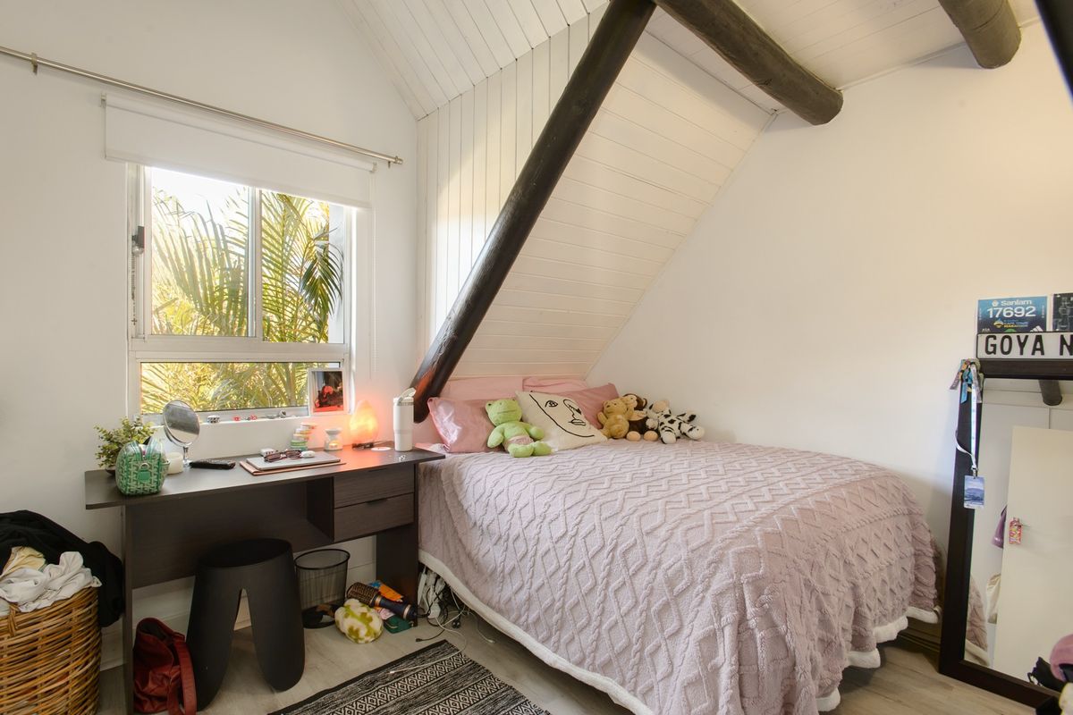 A cozy bedroom featuring a sloped ceiling with exposed timber beams, white paneling, and a window providing natural light.