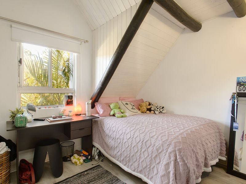 A cozy bedroom featuring a sloped ceiling with exposed timber beams, white paneling, and a window providing natural light.