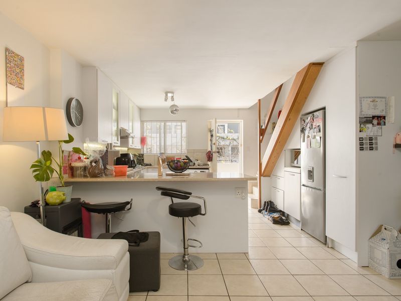 Open-plan living and kitchen area featuring tiled flooring, a breakfast bar, and a staircase leading to the upper level.