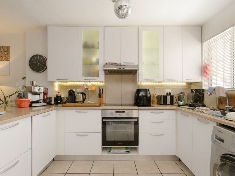 A functional kitchen featuring white cabinetry, under-cabinet lighting, integrated oven and hob, tiled backsplash, and tiled flooring with a built-in laundry appliance space.