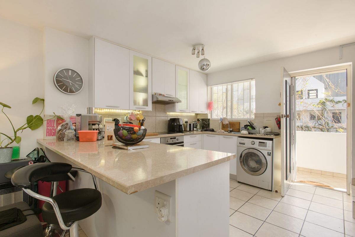 Functional kitchen featuring white cabinetry, stone countertops, a breakfast bar, integrated appliances, and direct access to an outdoor balcony area.
