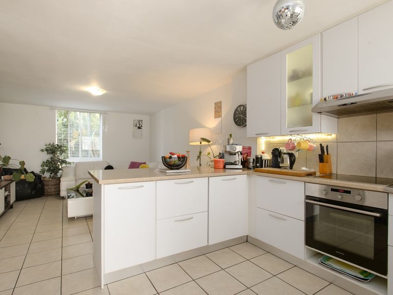 Open-plan living area featuring a modern kitchen with white cabinetry, integrated appliances, and tiled flooring throughout the combined space.