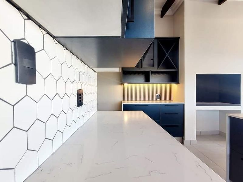Modern kitchen featuring sleek dark cabinetry, white quartz countertops, a stylish hexagon tile backsplash, and a built-in fireplace with integrated shelving.