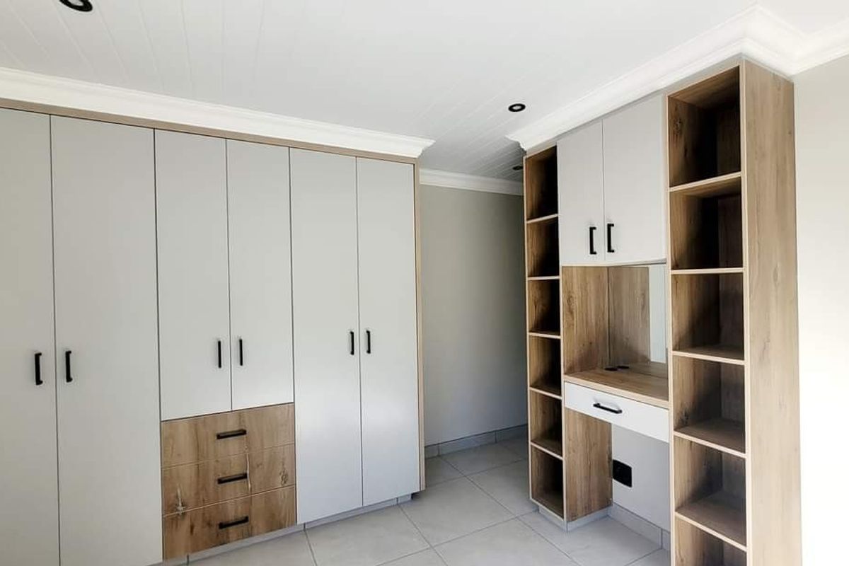 A modern bedroom featuring extensive built-in cabinetry with a integrated vanity desk, neutral tiled flooring, and a clean, contemporary finish.