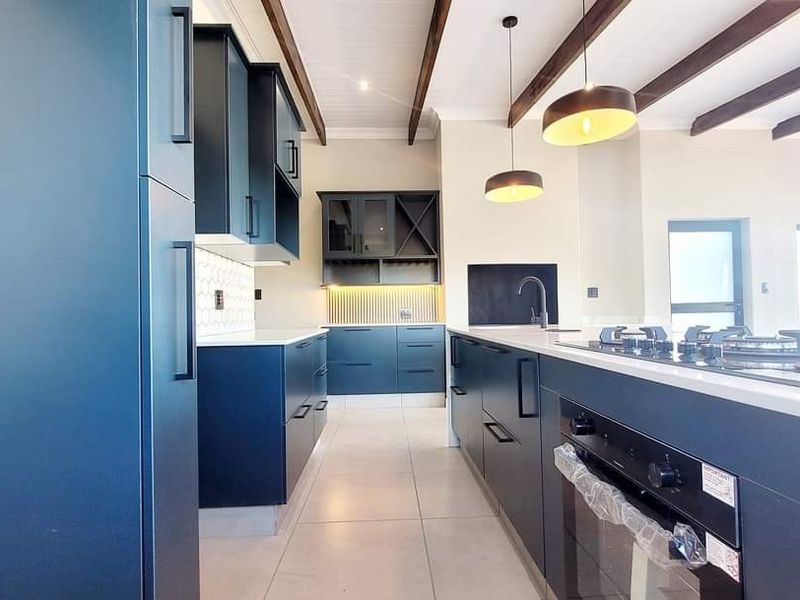 Modern kitchen featuring dark blue cabinetry, stone countertops, a central island with integrated gas cooktop and oven, and exposed timber ceiling beams.