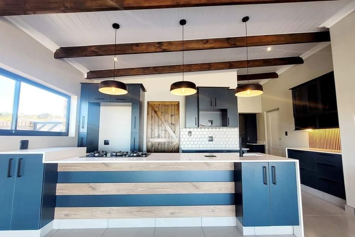 Modern kitchen featuring a large island with gas cooktop, dark blue and wood-tone cabinetry, stone countertops, and exposed timber ceiling beams.