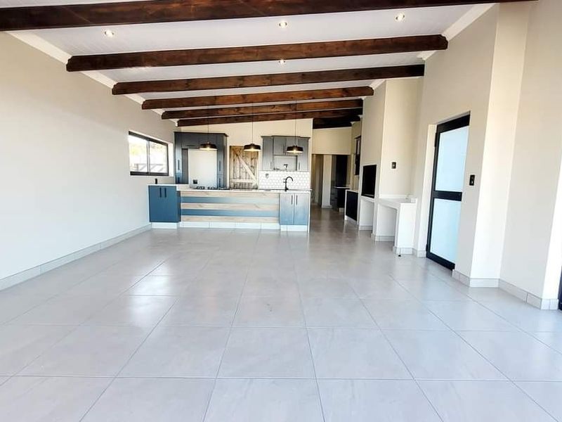 Spacious open-plan living and kitchen area featuring exposed timber ceiling beams, modern tiled flooring, and a built-in fireplace, offering a bright and versatile layout.