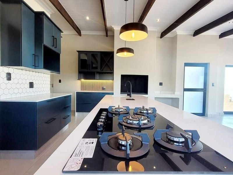 Modern kitchen featuring dark cabinetry, a large central island with a gas cooktop, stone countertops, and exposed ceiling beams.