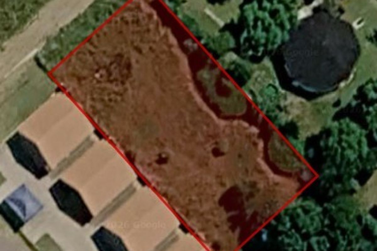 An aerial view of a vacant residential plot of land, outlined in red, situated within a developed neighborhood.