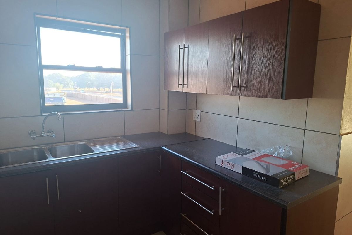 A clean, functional kitchen featuring dark wood-look cabinetry, a double stainless steel sink, and neutral wall tiling with ample natural light.