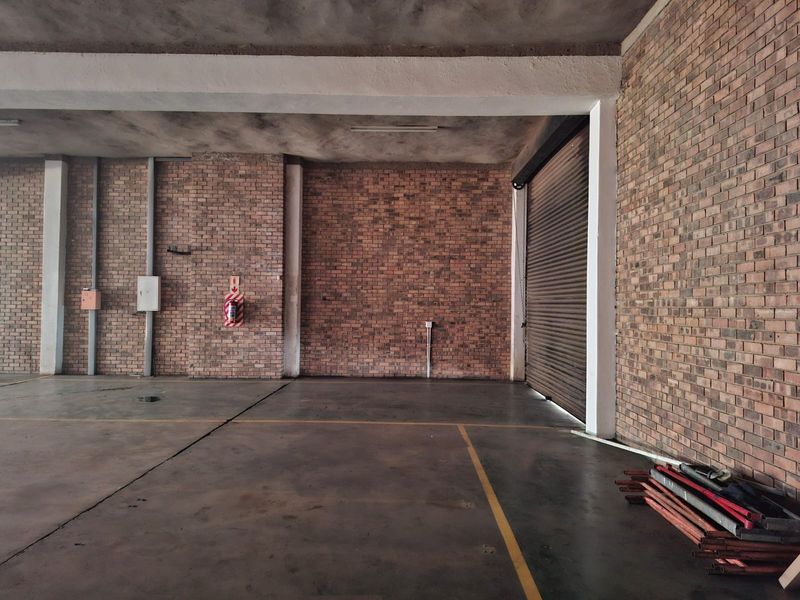 Spacious commercial garage featuring exposed brick walls, concrete flooring, and a secure roller shutter door, suitable for storage or workshop use.