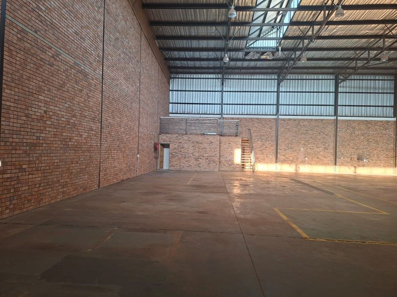 Spacious industrial warehouse unit featuring high ceilings with exposed steel trusses, large brick walls, concrete flooring, and a mezzanine level with staircase access.