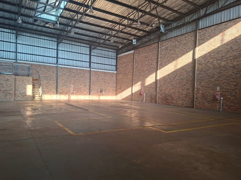 Spacious commercial warehouse or utility space featuring high ceilings, exposed brick walls, concrete flooring, and natural light from overhead skylights.