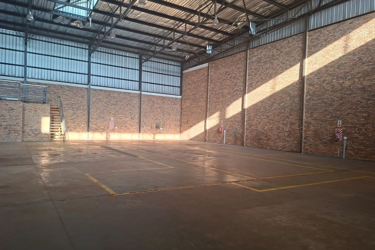 Spacious commercial warehouse or utility space featuring high ceilings, exposed brick walls, concrete flooring, and natural light from overhead skylights.