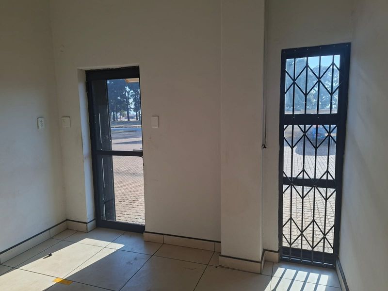 A vacant commercial entry area featuring tiled flooring, a glass door, and a security gate, providing direct access to the exterior.