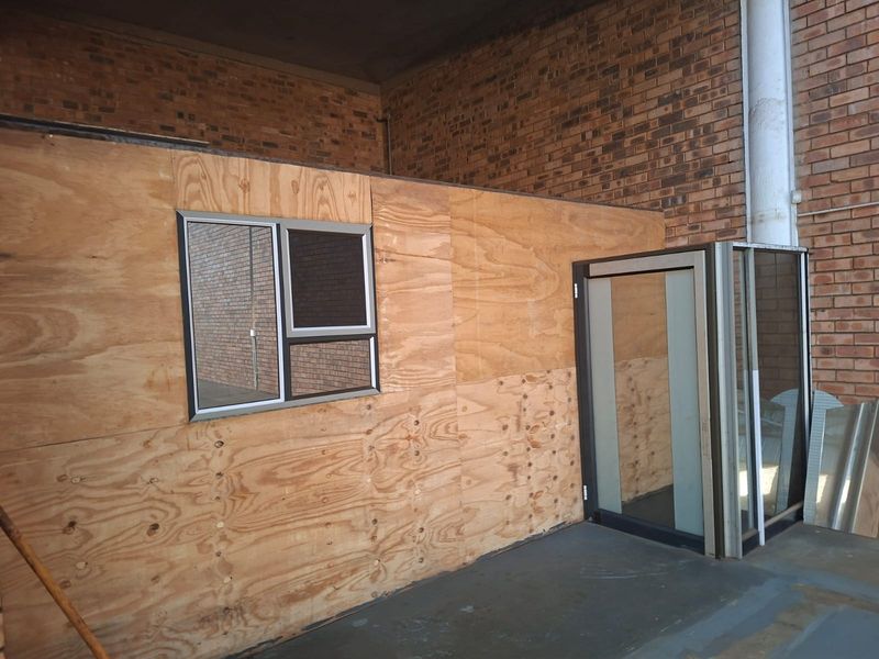 An unfinished utility or office space featuring exposed brick walls, concrete flooring, and a plywood partition wall with an integrated window and glass door.