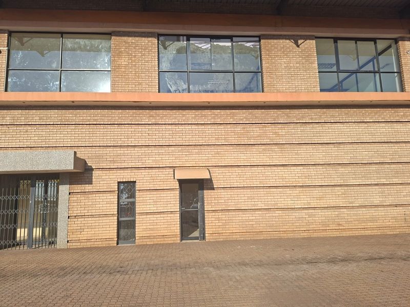 Front elevation of a commercial brick building featuring large aluminium windows, a secure entrance gate, and a paved exterior area.