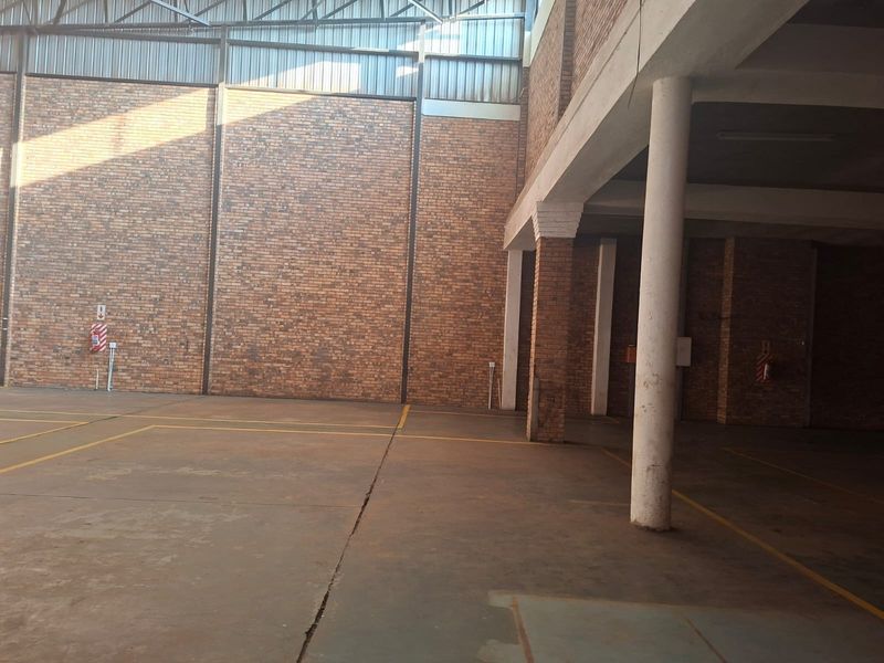 Spacious commercial utility area featuring exposed brick walls, concrete flooring, and high steel roof trusses, suitable for storage or industrial use.