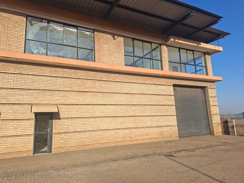 Commercial warehouse exterior featuring a face brick facade, large roller shutter door, and upper-level aluminium framed windows with a paved driveway.