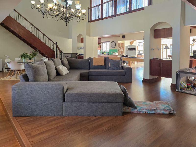 Spacious open-plan living area featuring a grand wooden staircase, mezzanine level, and arched architectural details connecting to the kitchen and dining spaces.