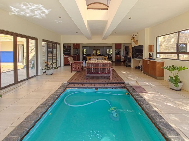 Unique indoor pool area featuring a central swimming pool, wooden decking, skylight, and built-in braai, seamlessly connected to the living space via sliding doors.