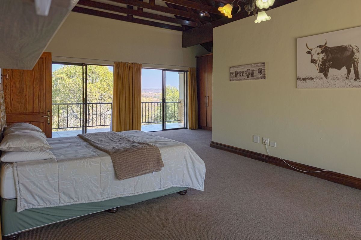 Spacious bedroom featuring exposed timber ceiling beams, built-in cupboards, and sliding glass doors leading to a private balcony with scenic views.