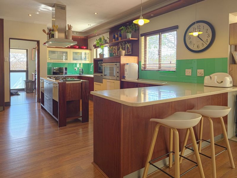 Modern kitchen featuring a central island with gas hob, built-in appliances, breakfast bar seating, and vibrant green glass splashbacks.