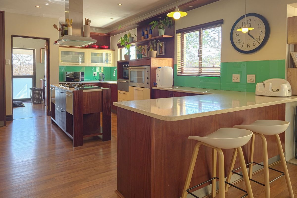 Modern kitchen featuring a central island with gas hob, built-in appliances, breakfast bar seating, and vibrant green glass splashbacks.