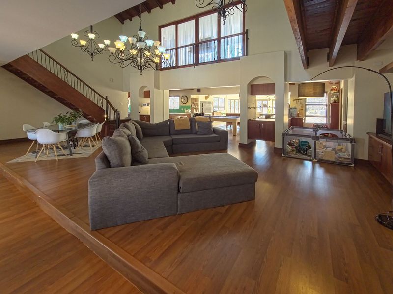 Spacious open-plan living area featuring high vaulted ceilings with exposed timber beams, a grand staircase, and a mezzanine level overlooking the main floor.