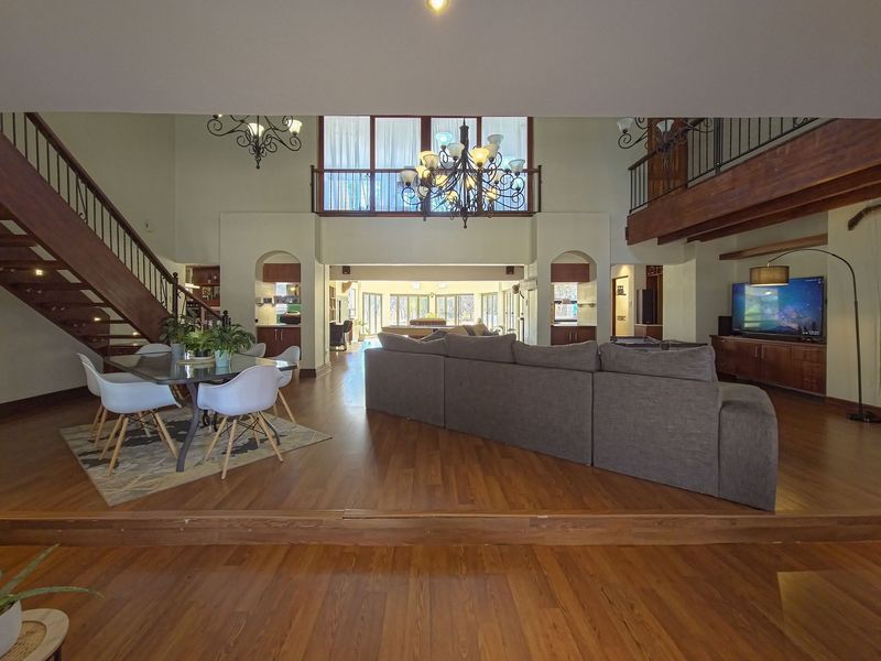 Spacious open-plan living area featuring hardwood floors, a grand wooden staircase, mezzanine level, and elegant architectural arches with built-in cabinetry.