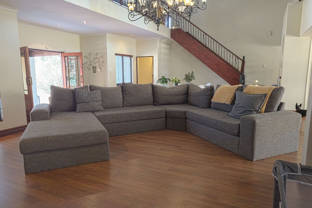 Spacious open-plan living area featuring double-volume ceilings, a wooden staircase with wrought iron balustrade, and laminate flooring with access to the outdoors.