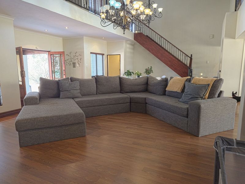 Spacious open-plan living area featuring double-volume ceilings, a wooden staircase with wrought iron balustrade, and laminate flooring with access to the outdoors.
