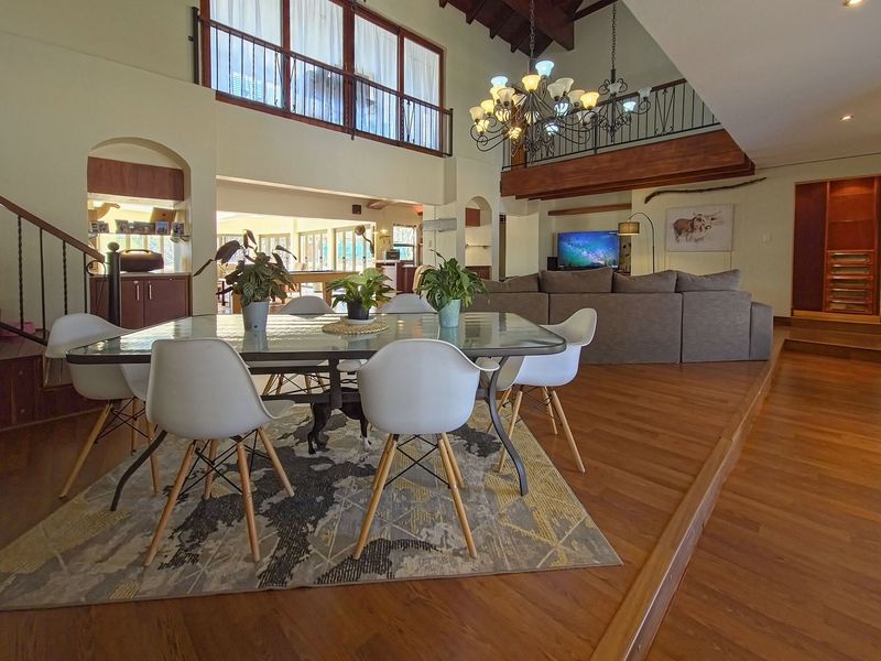 Spacious open-plan living and dining area featuring a vaulted timber ceiling, mezzanine level with wrought iron railings, and warm hardwood flooring.