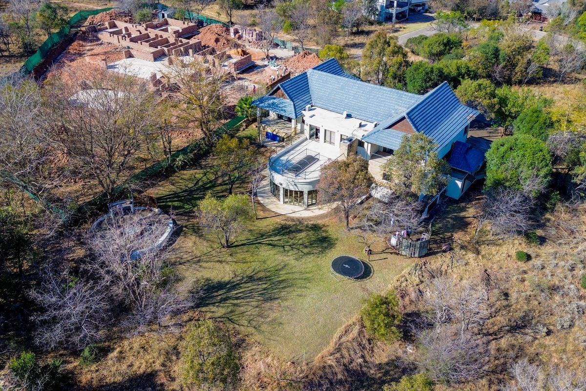 Aerial view of a large residential property featuring a tiled roof, spacious balcony, patio area, swimming pool, and expansive surrounding garden grounds.
