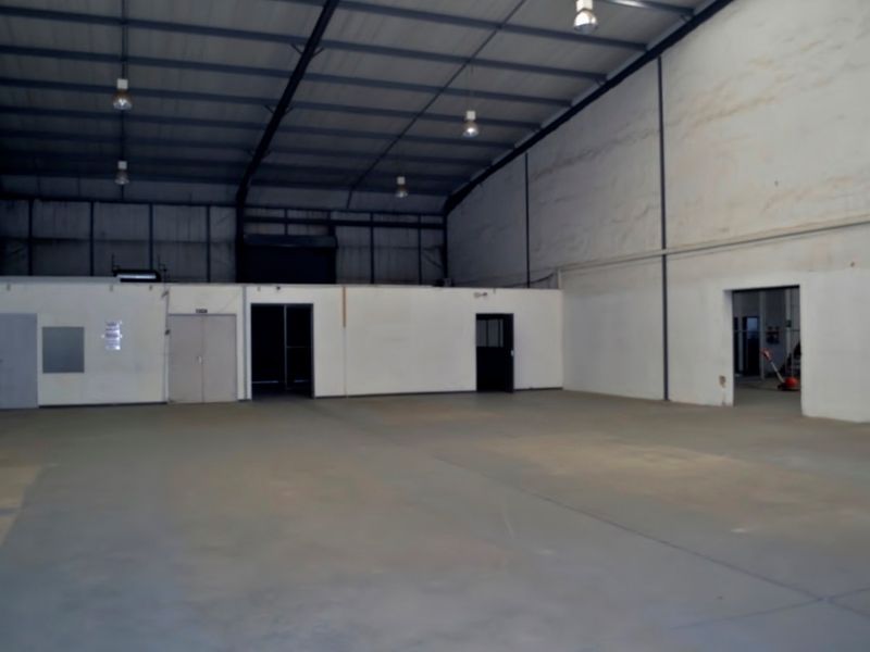 Spacious industrial warehouse featuring high ceilings, concrete flooring, and integrated office partitioning, suitable for storage or manufacturing operations.