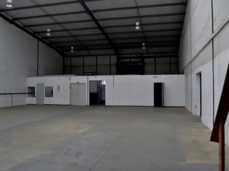 Spacious industrial warehouse unit featuring high ceilings with exposed steel trusses, concrete flooring, and integrated internal office or storage partitioning.